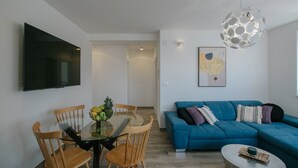 A modern living room with a blue sofa, a glass dining table with chairs, a TV mounted on the wall, and a unique ceiling light fixture. - Spacious Luxury Trogir Apartments - Superior Two Bedroom Apartment (Trogir)