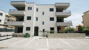 A modern multi-story building with a flat facade, balconies, and a parking lot in front. - Spacious Luxury Trogir Apartments - Superior Two Bedroom Apartment (Trogir)