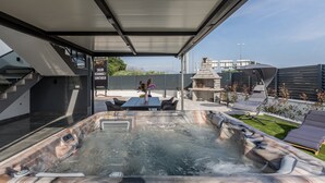 Un área moderna para jacuzzi al aire libre, con techo cubierto, mesa y sillas, y una parrilla para barbacoa.
