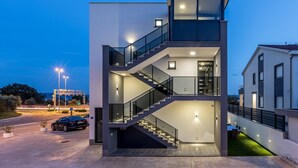 Un edificio moderno de dos pisos con una escalera de cristal, una terraza en la azotea y una entrada bien iluminada.