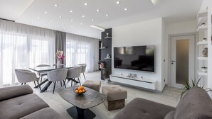 A modern living room with a large flat-screen TV, a dining area with a glass table, and a sofa set.