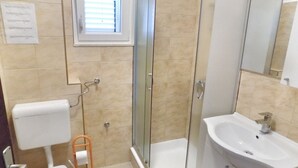 Une salle de bain comprenant des toilettes, une douche à parois de verre, un lavabo et une fenêtre.