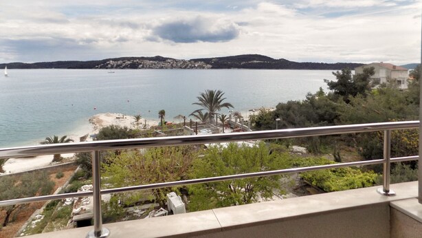 A coastal view from a balcony with a railing, overlooking a beach, a body of water, and a distant hill with buildings. - Trogir Sunny Apartments with Sea View - Standard Two bedroom Apartment with Sea view and Balcony (Trogir)