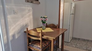 Un coin repas avec une table et des chaises en bois, un vase rempli de fleurs et une fenêtre avec des stores.