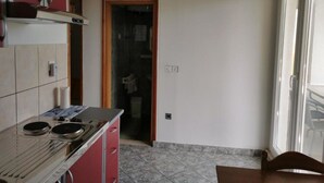 Une cuisine équipée d’une cuisinière, d’un évier et de placards, donnant sur une salle de bain avec douche et toilettes.