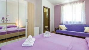 A hotel room with a bed, a sofa, a mirror, and a window with curtains.