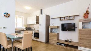 A modern kitchen with white cabinets, a dining area with a glass table and chairs, and a TV mounted on the wall.