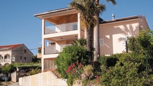 A multi-story building with balconies, surrounded by lush greenery and a palm tree. - Holiday Home Boni - Holiday Home (Rab)
