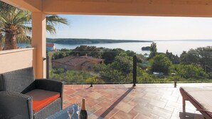 A balcony with a view of a lake, wicker furniture, and a tiled floor. - Holiday Home Boni - Holiday Home (Rab)