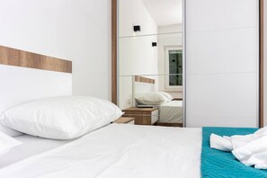 Moderni hotellihuone, jossa on suuri sänky, yöpöytä ja peili, joka heijastaa huonetta.
