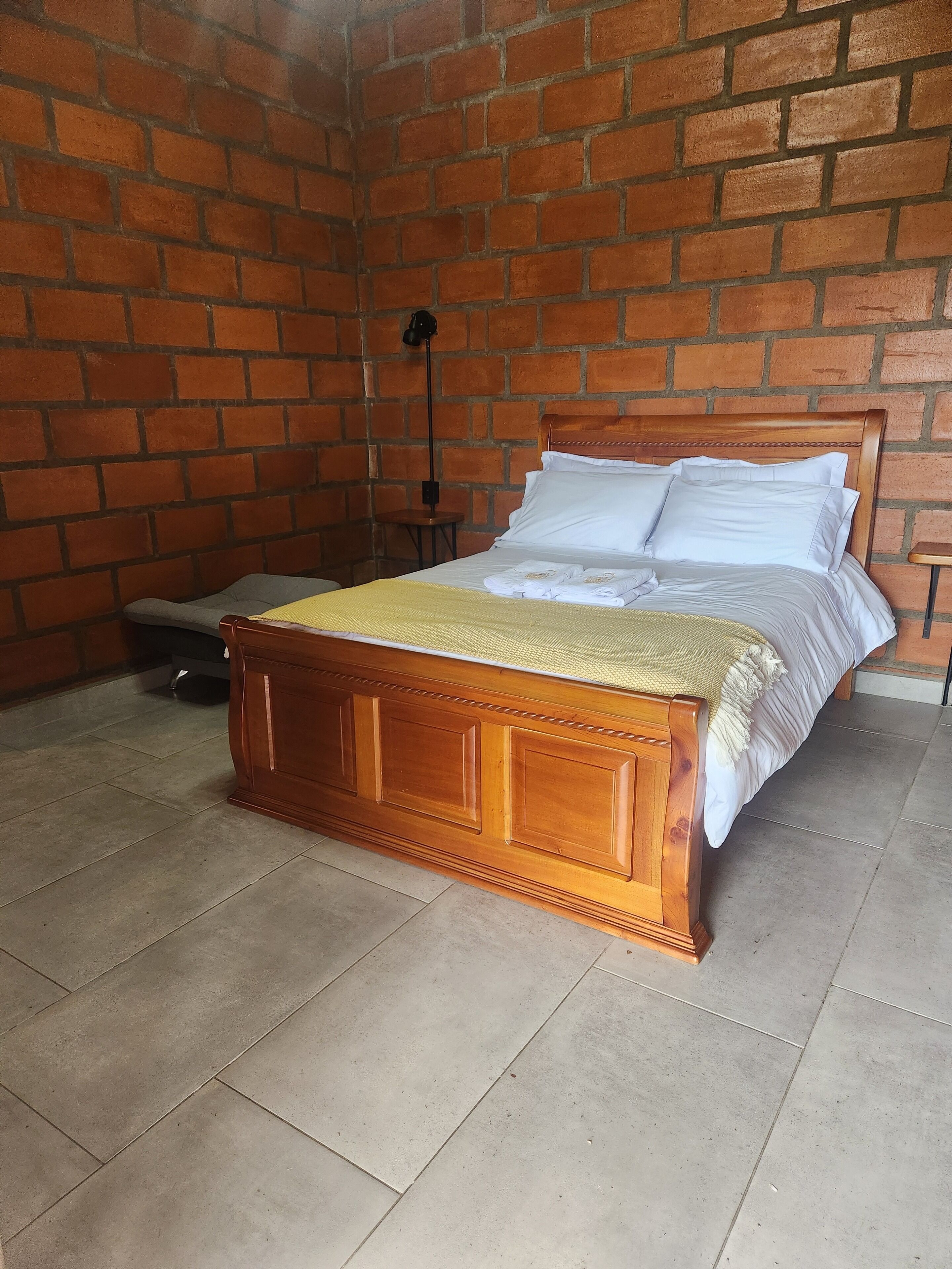 Una cama de madera con ropa de cama blanca en una habitación con pared de ladrillo.