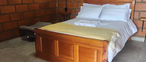 Una cama de madera con ropa de cama blanca en una habitación con pared de ladrillo.