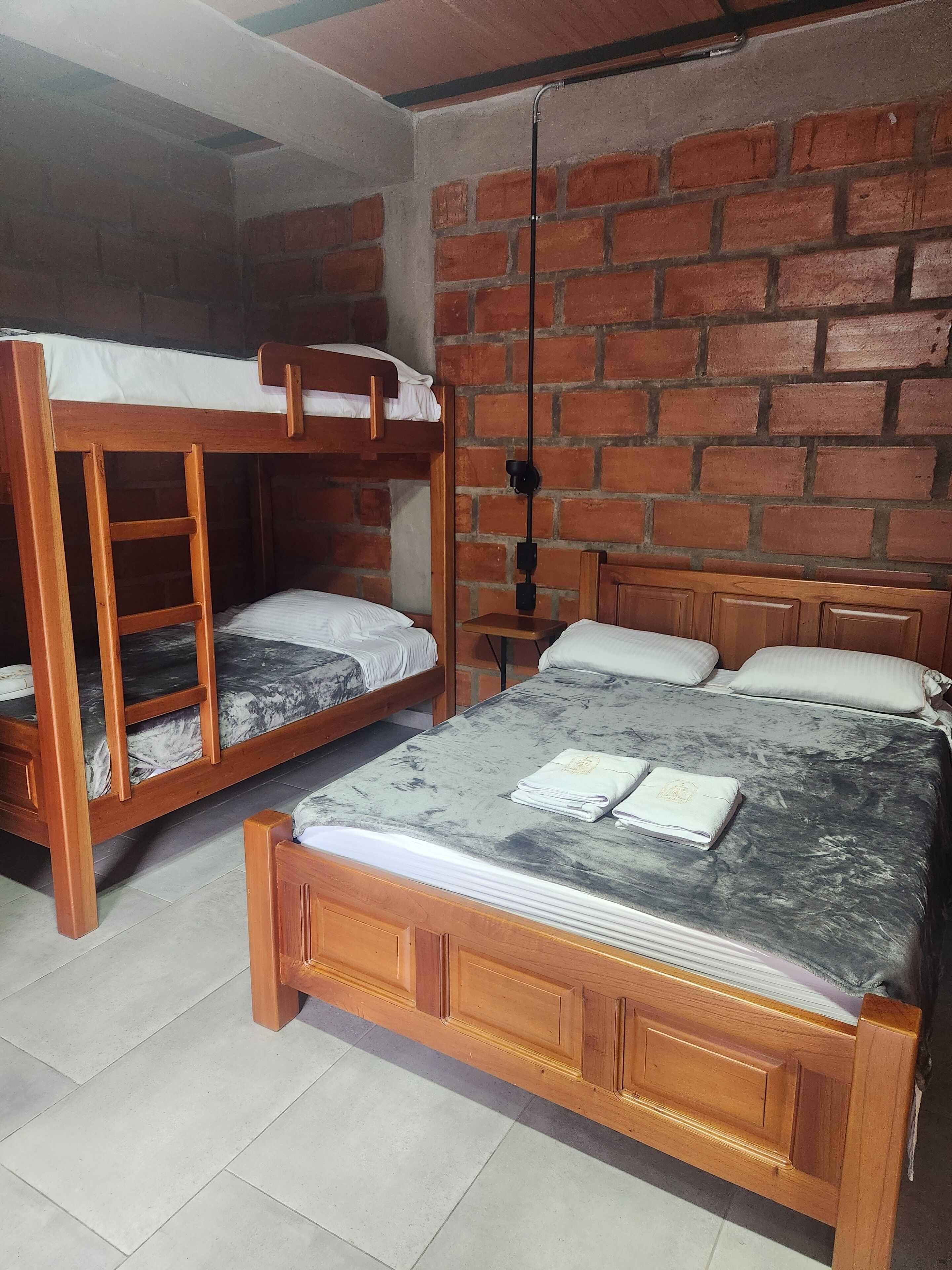 A room with two wooden bunk beds, a single bed, and a brick wall.