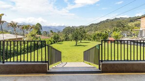 Vista da un balcone con una scala che conduce a una zona erbosa, circondata da alberi e una catena montuosa sullo sfondo.