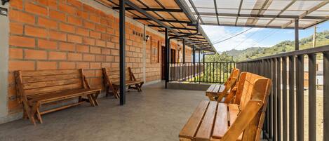 Un patio cubierto con bancos y mesas de madera, paredes de ladrillo y barandilla metálica con vistas panorámicas.