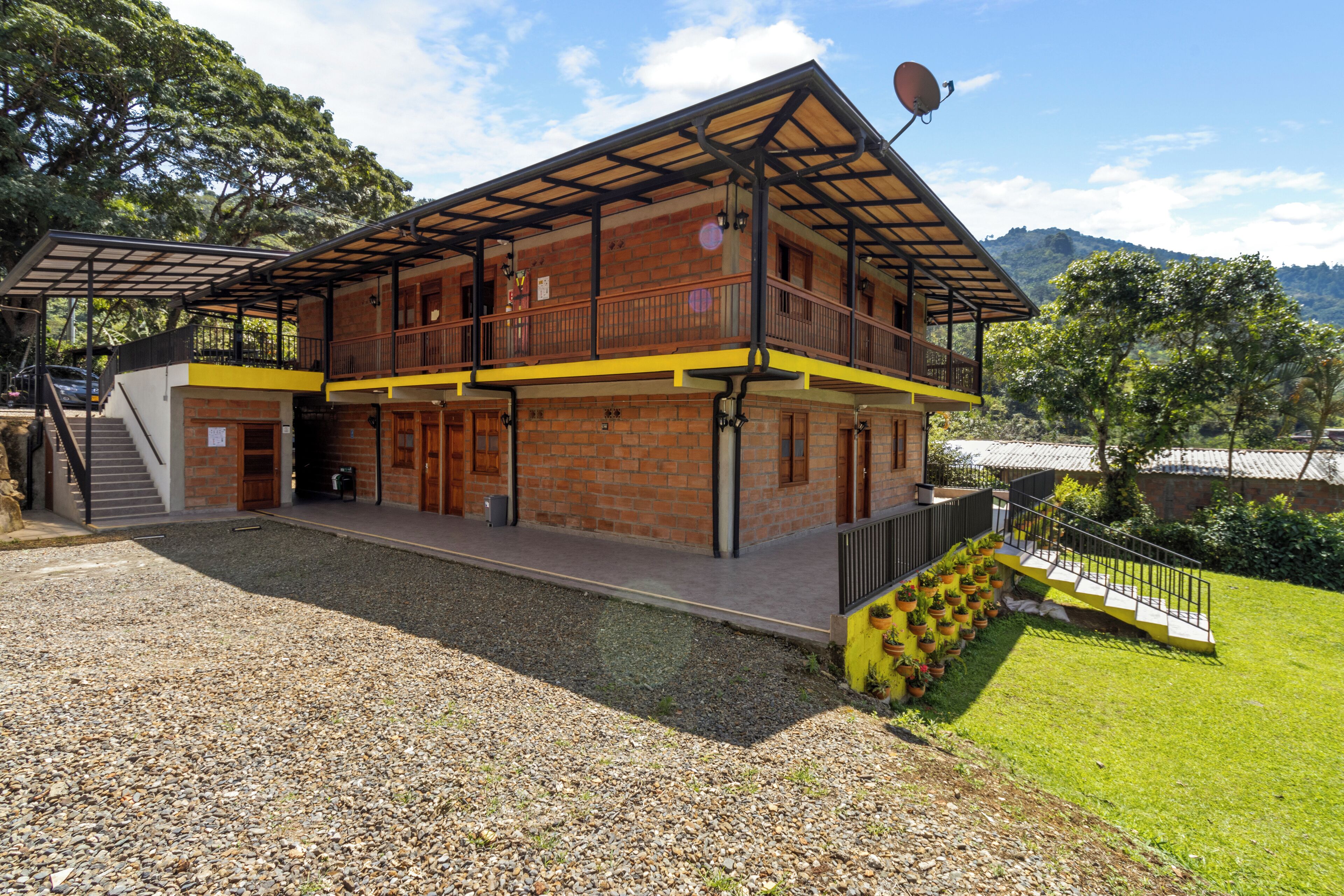 Un edificio a due piani con un balcone, un vialetto sterrato e una zona verde con piante in vaso.