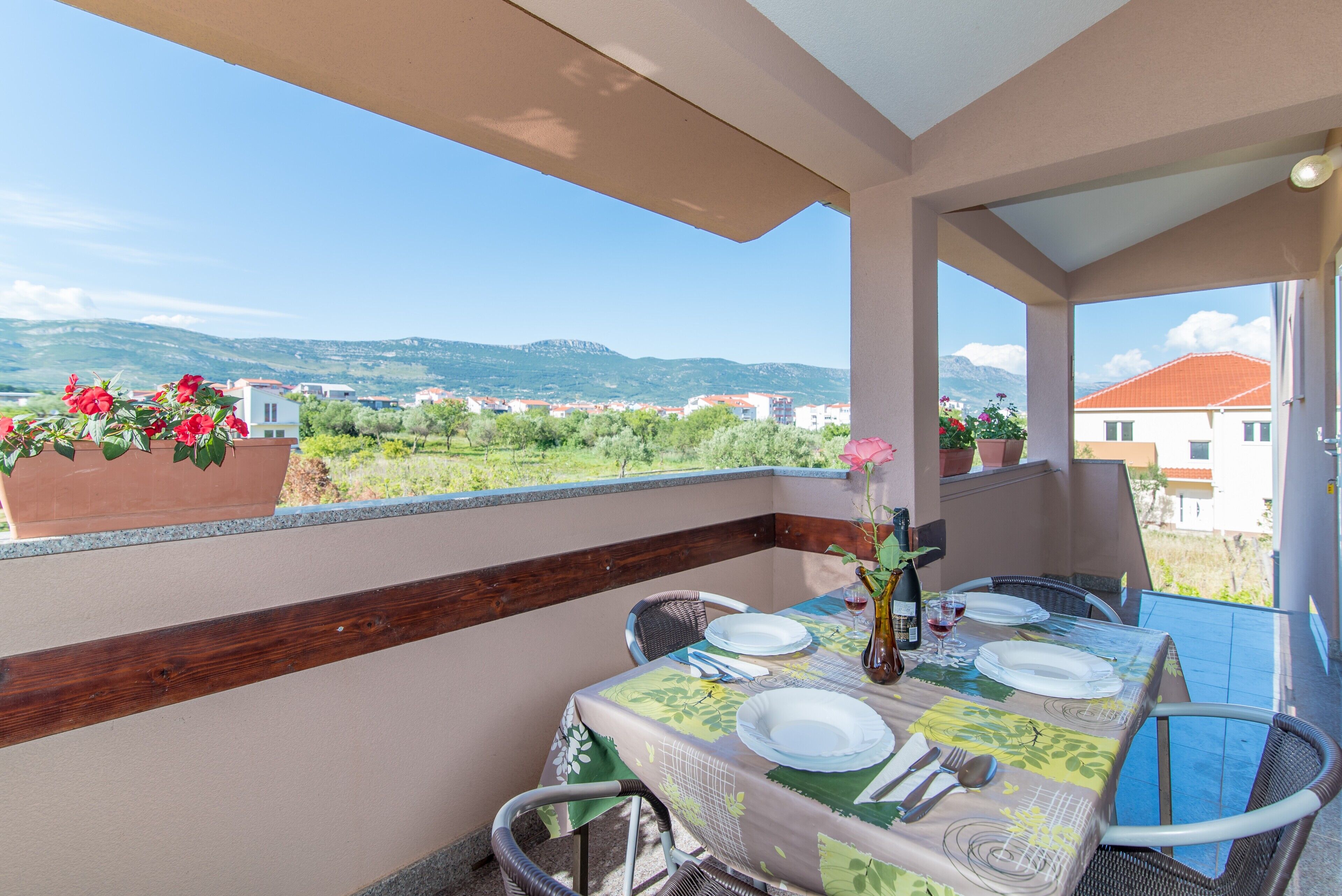 A balcony with a table set for dining, overlooking a scenic landscape with buildings and mountains.