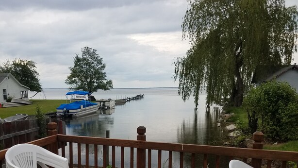 Eine Terrasse mit Blick auf einen ruhigen See, ein Steg mit einem Boot und ein Holzzaun.