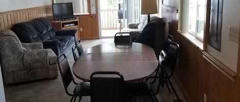 A dining area with a round table and chairs, a sofa, a television, and a ceiling fan.