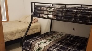 Ein Stockbett mit karierter Bettdecke und ein einfaches Bett mit einer Steppdecke.