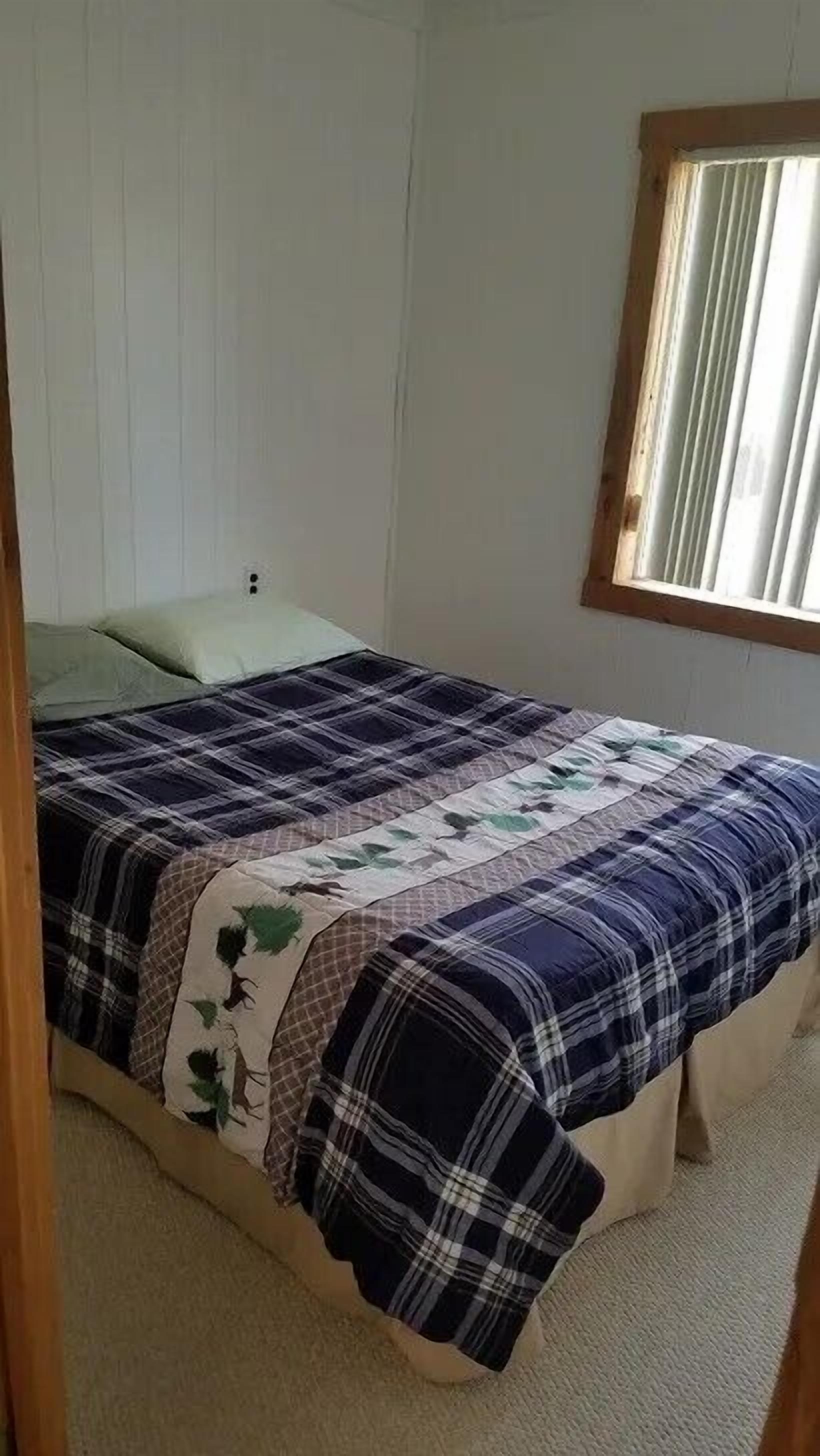 Een slaapkamer met een bed, een raam met gordijnen en een deur.