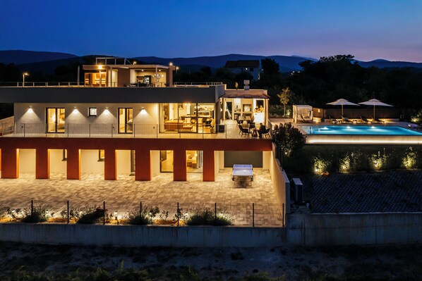 Ein modernes, zweistöckiges Haus mit Swimmingpool, Außenbereich zum Sitzen und einer gut beleuchteten Terrasse.