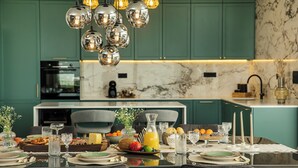 Une cuisine moderne avec des meubles de couleur turquoise, un plan de travail en marbre et un coin repas aménagé pour prendre un repas.