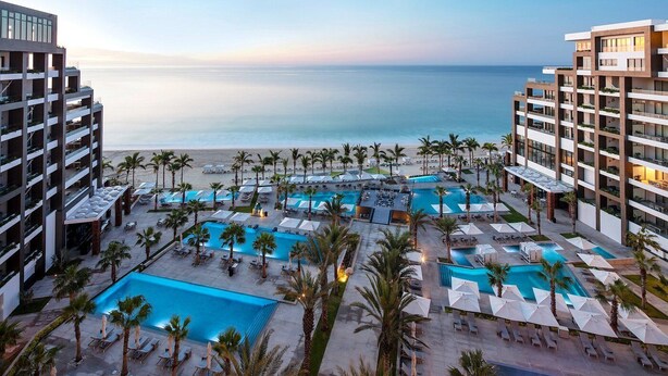 Ein Resort mit mehreren Pools, Palmen und Blick auf den Strand.