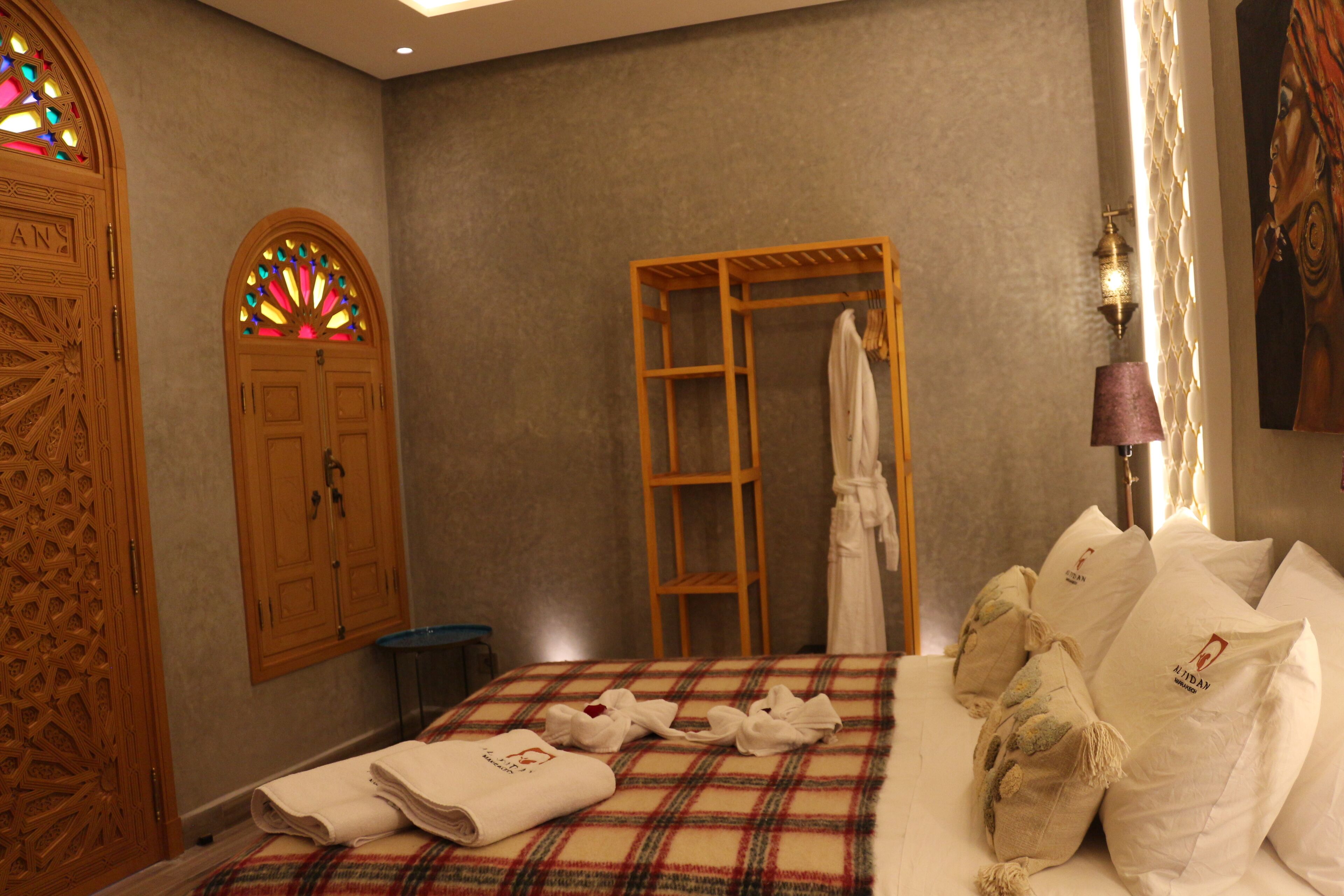 Une chambre d’hôtel avec un lit, une armoire en bois, un vitrail et une lampe fixée au mur.