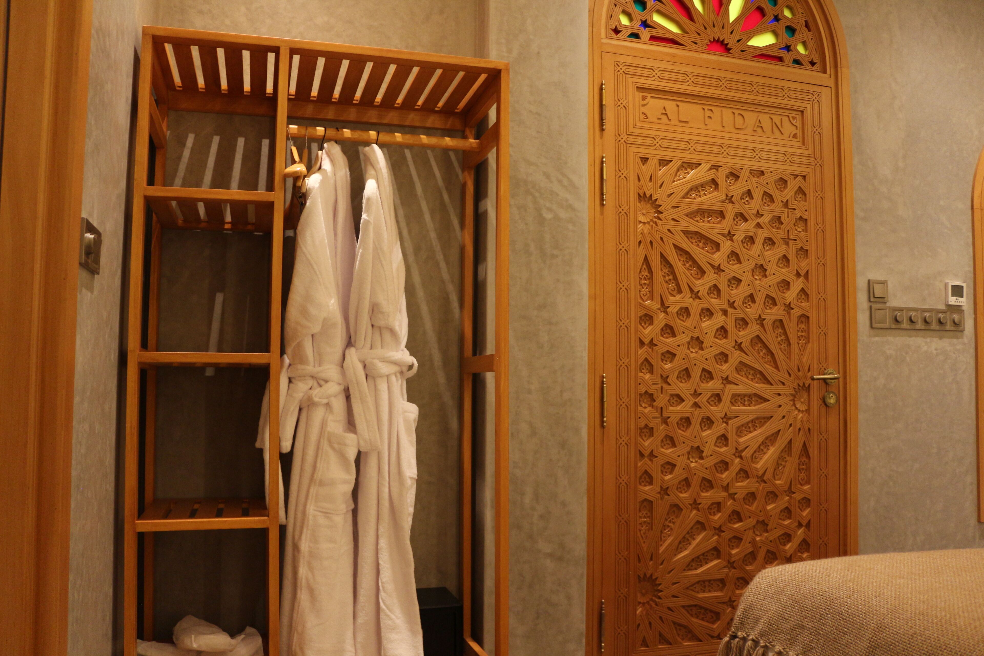 Une armoire en bois dotée d’une tringle pour suspendre les vêtements, une porte ornée de sculptures complexes et un lit recouvert d’une couverture à motifs.