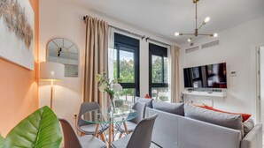 A modern living room with a glass dining table, grey sofa, and a TV mounted on the wall. - Modern 2-bedroom duplex apartment near Historical center (Málaga)