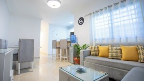 A modern living room with a sofa, chairs, a glass coffee table, and a water dispenser.