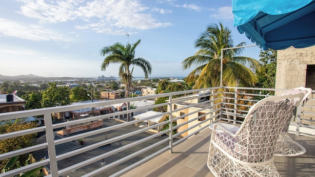 A balcony with a white metal railing, a white woven chair, and a blue awning.