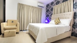 A hotel room with a bed, a chair, an air conditioning unit, and a patterned wall.