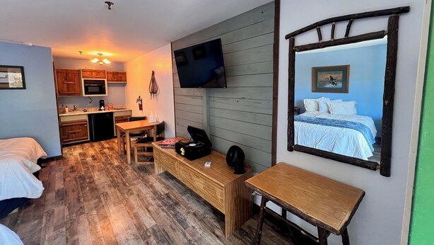 A compact hotel room with a kitchenette, a bed, a desk, and a large mirror.