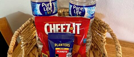 A basket containing two bottles of Pure Life water, a bag of Cheez-It, a bag of Planters salted peanuts, and a Quaker Chewy peanut butter chocolate chip bar.