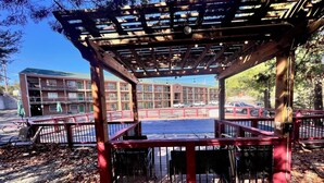 A gazebo with a wooden structure and metal railings, surrounded by fallen leaves and a parking lot with cars.