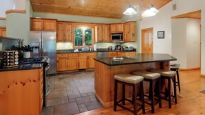 Una cocina amplia con armarios de madera, una isla grande con taburetes de bar, electrodomésticos de acero inoxidable y vistas a zonas verdes.