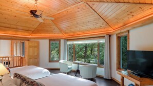 Un dormitorio espacioso con dos camas, un escritorio, una silla, un televisor y ventanas amplias que ofrecen vistas al exterior.