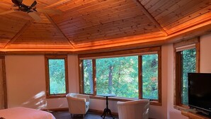 Ein Blockhauszimmer mit zwei Betten, einem Fernseher, einem Tisch und großen Fenstern mit Blick auf den Wald.