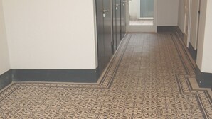 A hallway with patterned flooring, a door with a sign, and a view into another room. - Apartment with terrace in a great city location 45 m2, only 2 minutes to subway (Wien)