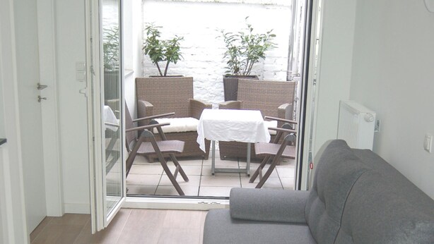A room with a grey sofa, a sliding glass door leading to an outdoor patio with wicker furniture and a table. - Apartment with terrace in a great city location 45 m2, only 2 minutes to subway (Wien)