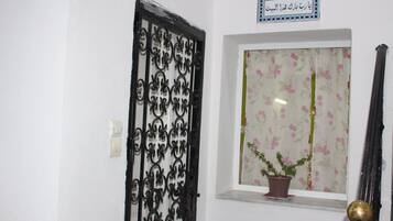 Une porte ornée de motifs complexes en métal noir, un pot de fleurs posé sur un rebord de fenêtre et une enseigne avec du texte en arabe.