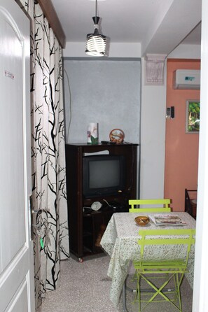 A room with a television, a table with a tablecloth, and a green chair.