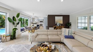 A spacious living area with a beige sectional sofa, a coffee table with decorative items, and a view of a kitchen and dining area.
