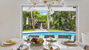 A dining area with a table set for four, overlooking a swimming pool and lush garden.