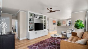 A modern living room with a flat-screen TV, white cabinets, a ceiling fan, and a large plant. - Solace in South Austin - Game Room (Austin)