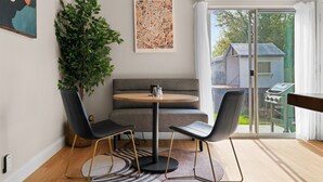 A dining area with a round table, two chairs, a bench, a potted plant, and a cityscape view through a glass door. - Solace in South Austin - Game Room (Austin)