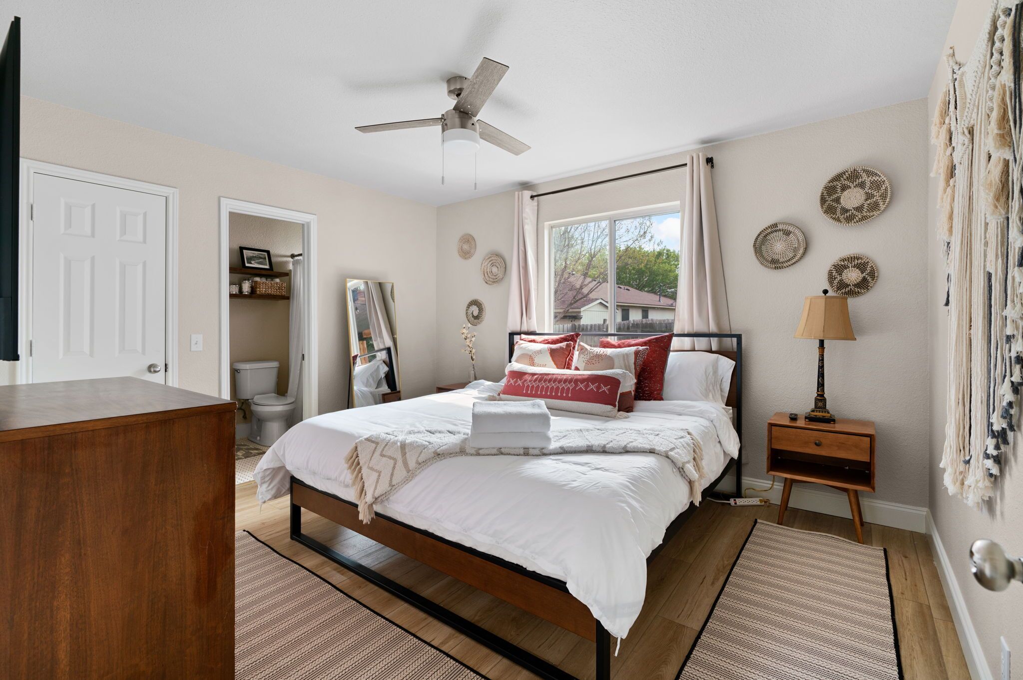 A bedroom with a bed, a nightstand, a ceiling fan, a window with curtains, and a door.