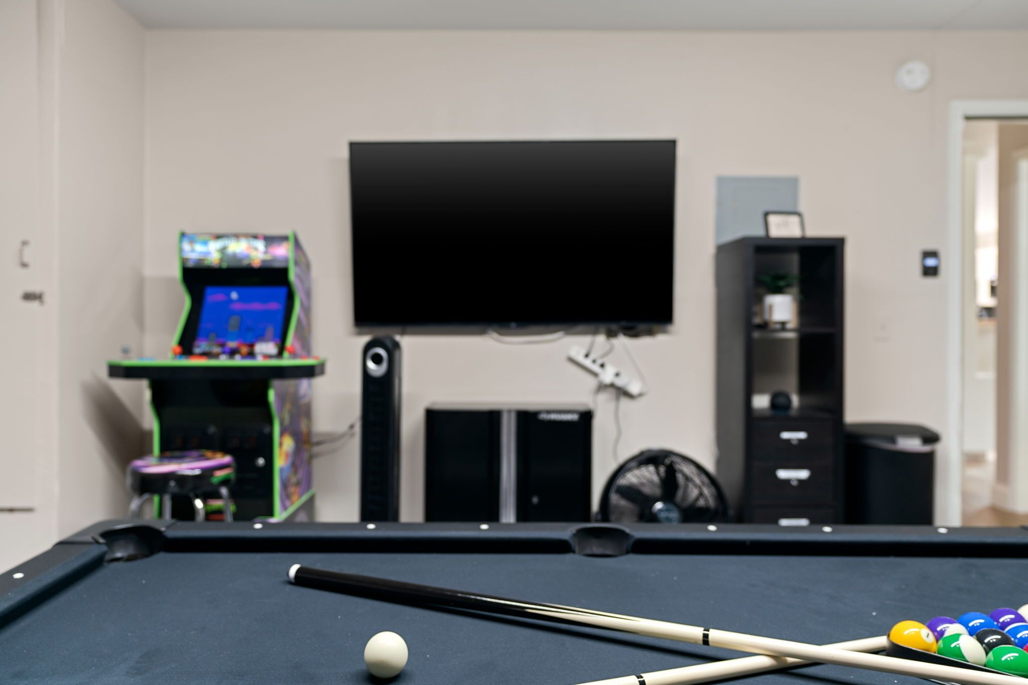 Een pooltafel met een witte bowlingbal en twee stokken, een televisie aan de muur en een kleine speelautomaat op de achtergrond.
